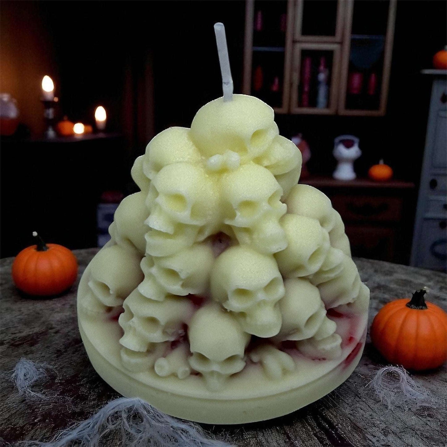 Bleeding Skulls Candle with red wax details, gothic Halloween skull decor on wooden table with small pumpkins and spooky background.