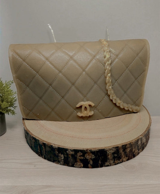 Luxe Couture Purse Candle shaped like a beige quilted designer handbag with gold-tone chain, displayed on a wooden slice.