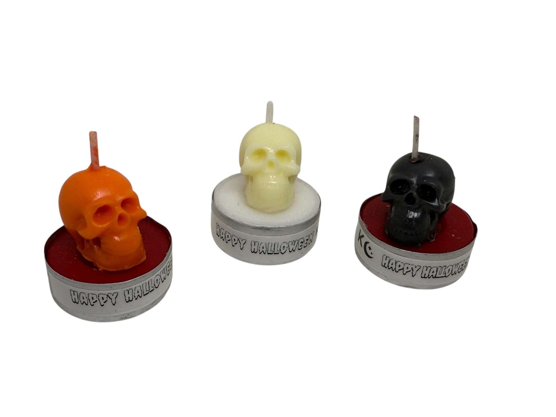 Set of three skull tealight candles in orange, white, and black colors with "Happy Halloween" text on metal bases for spooky Halloween décor.